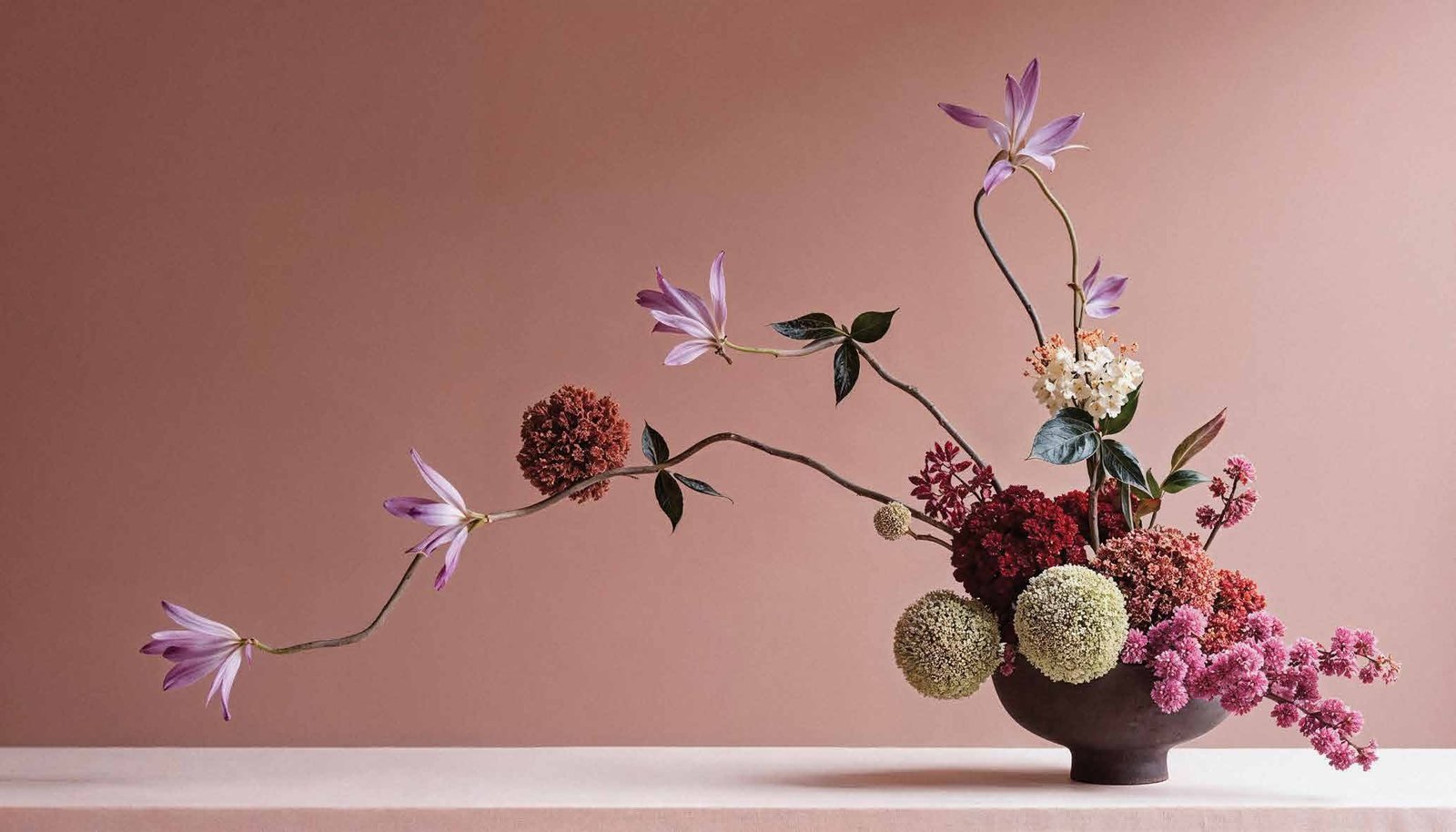 Modern ikebana-style floral arrangement against a dusty rose wall